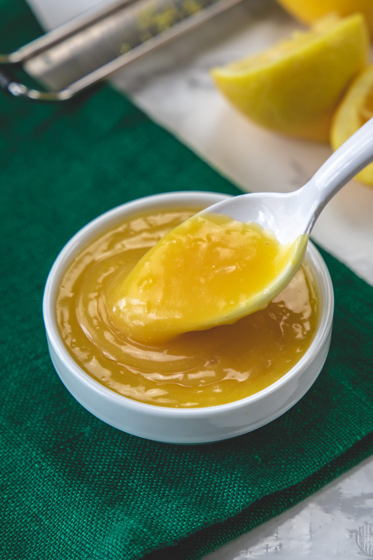 Spoonful of eggless lemon curd taking from the bowl with green napkin under the bowl.