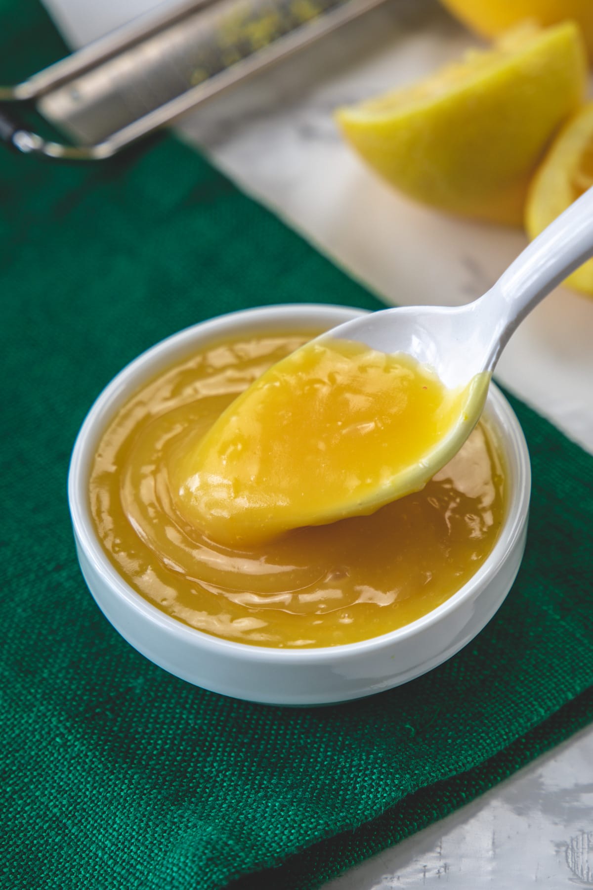 Spoonful of eggless lemon curd taking from the bowl with green napkin under the bowl.