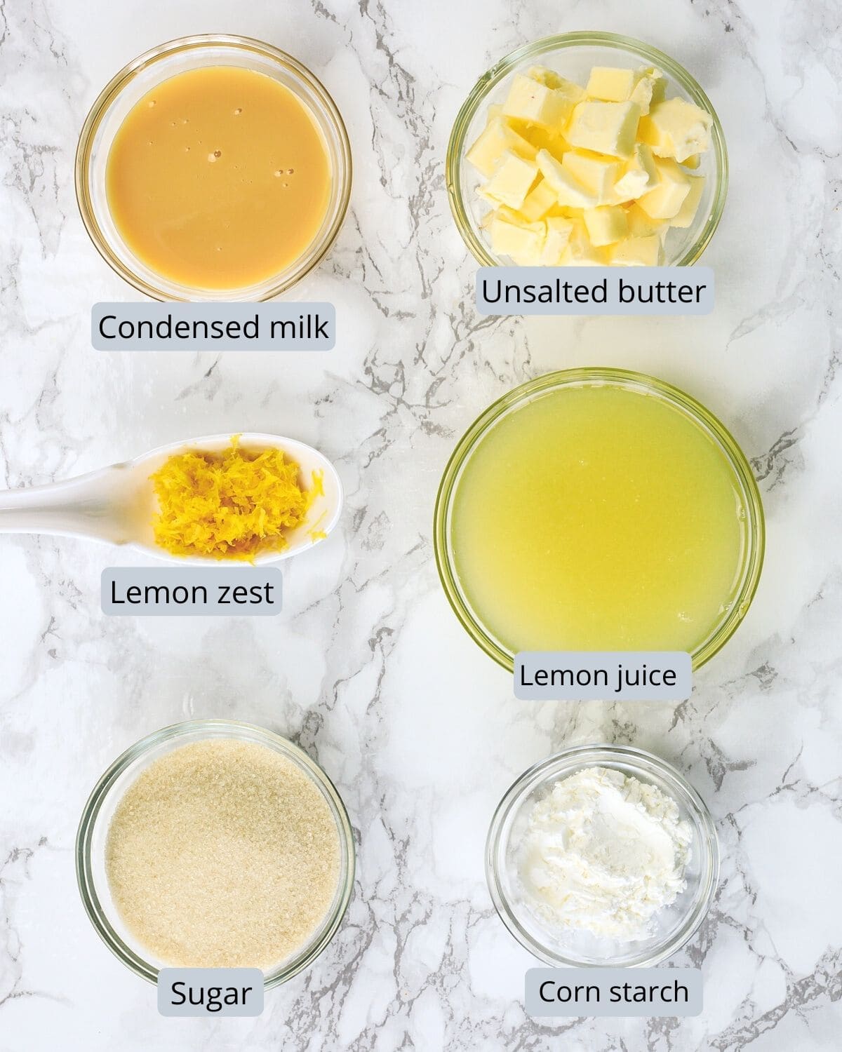 Eggless lemon curd ingredients are in individual bowls on a marble surface.