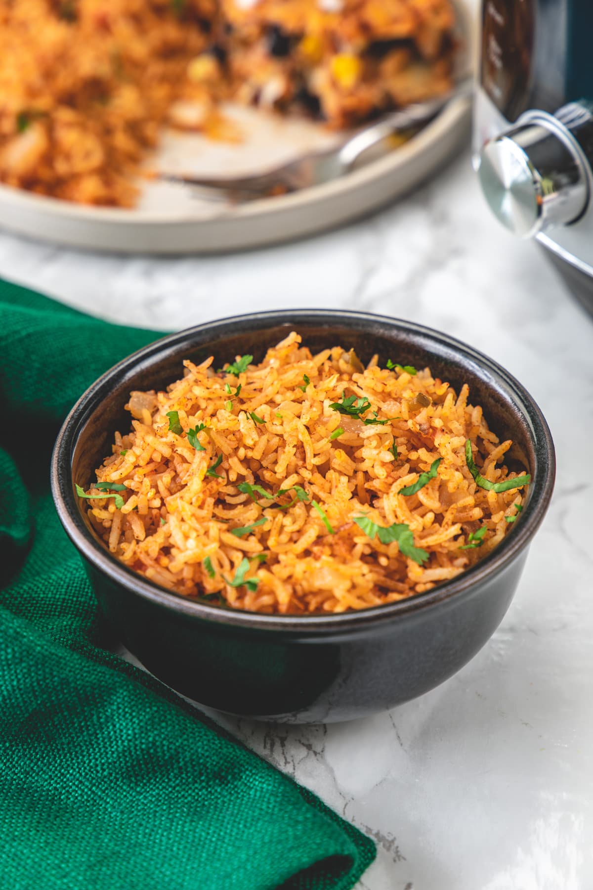 Mexican rice in a black bowl with green napkin on left and instant pot on right side.