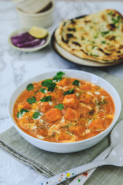 Paneer butter masala garnished with cream and cilantro on the napkin served with naan and onions.