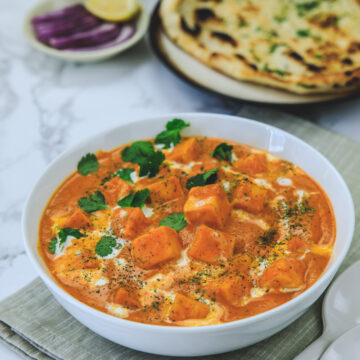 Paneer butter masala garnished with cream and cilantro on the napkin served with naan and onions.