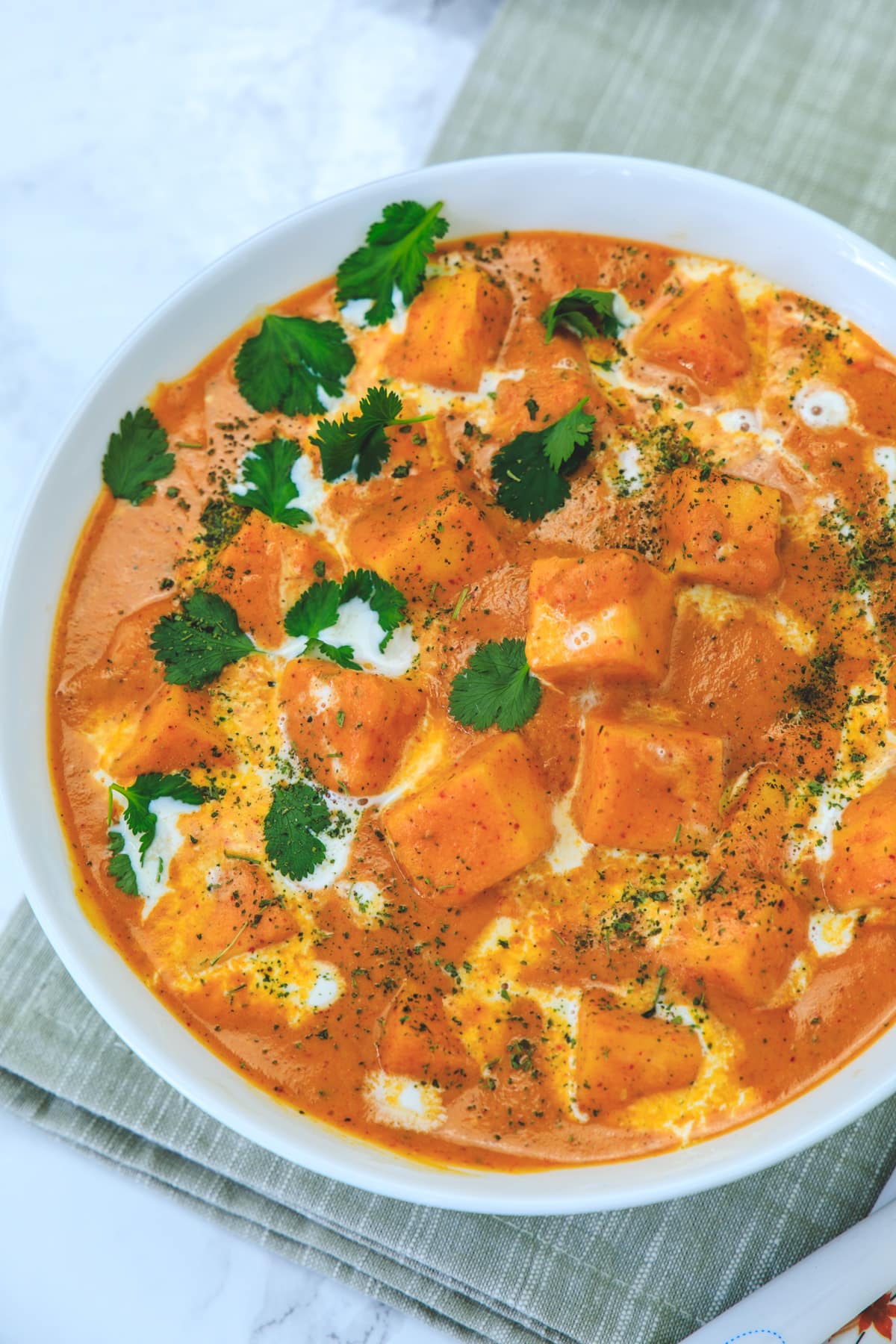 Close up of paneer butter masala in a bowl garnished with cream, cilantro and kasoori methi.