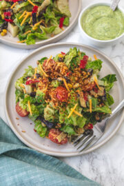 Vegetarian taco salad served in a plate with fork and another salad plate in the back with dressing in a bowl.