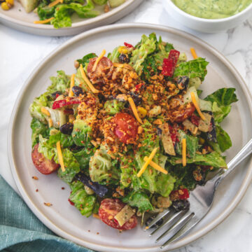 Vegetarian taco salad served in a plate with fork and another salad plate in the back with dressing in a bowl.