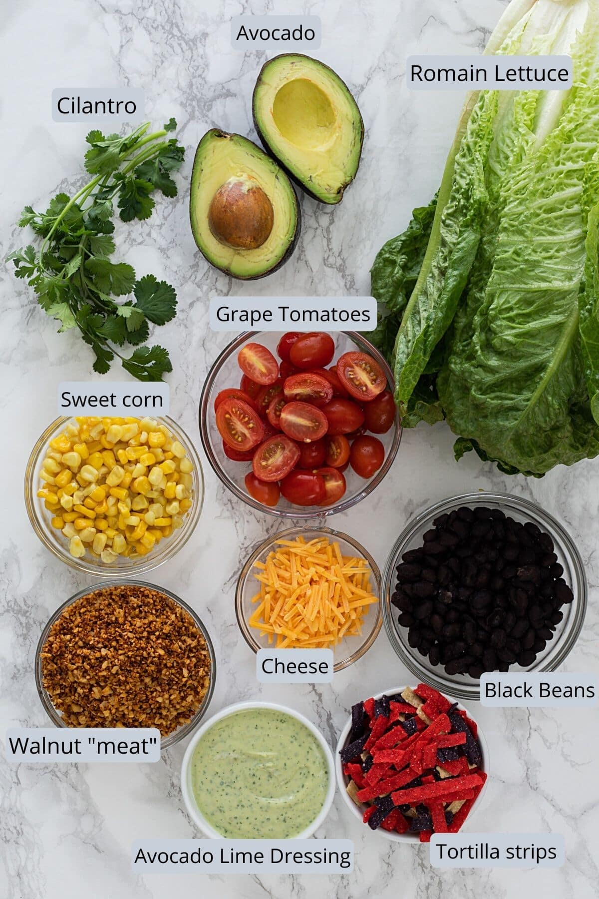 Ingredients used in vegetarian taco salad in individual bowls on marble surface.