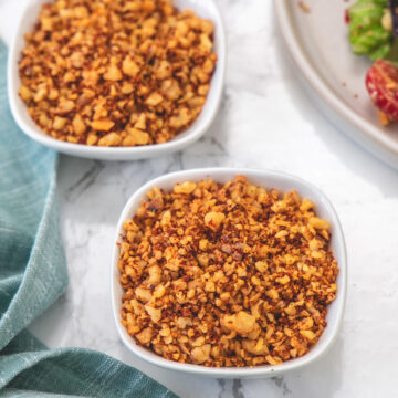 Vegan walnut meat in 2 white bowls with napkin on side and salad plate in the back.