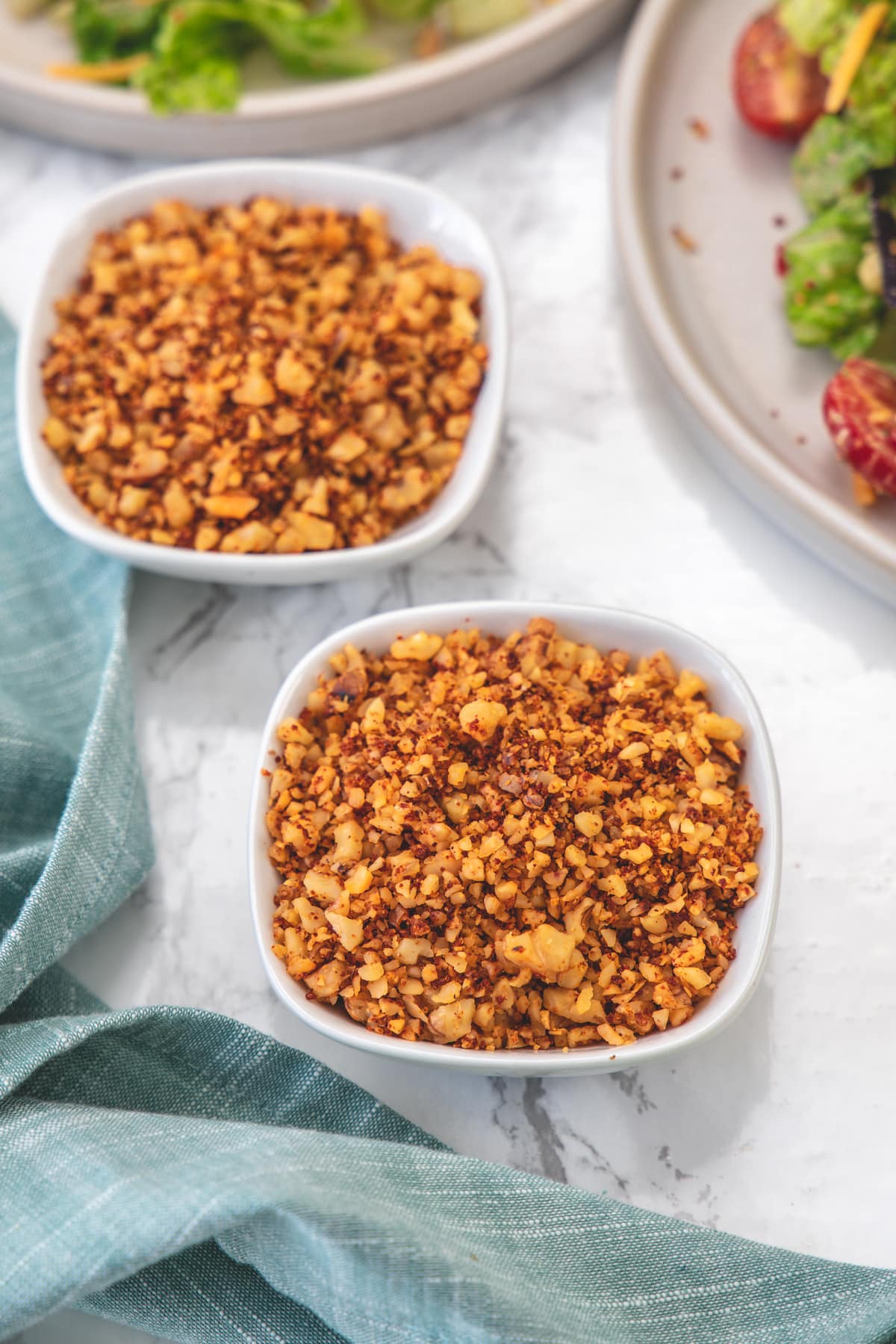 Vegan walnut meat in 2 white bowls with napkin on side and salad plate in the back.