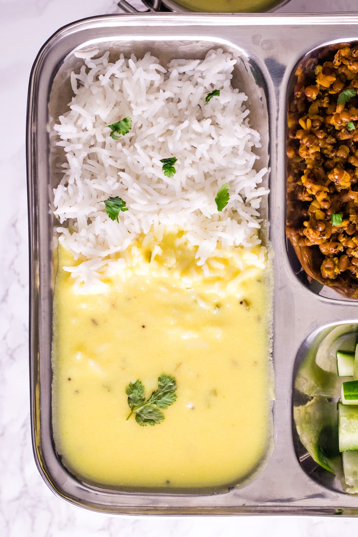 Gujarati kadhi served with rice in a steel plate.