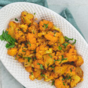 Aloo gobi masala served in an oval platter and garnished with cilantro.