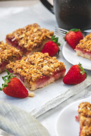 Strawberry cake squares on marble with few strawberries place around.