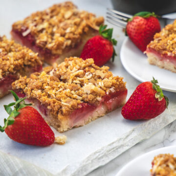 Strawberry cake squares on marble with few strawberries place around.