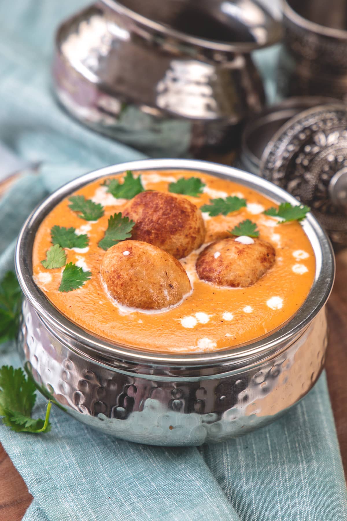 Malai kofta served in steel bowl with napkin underneath. 