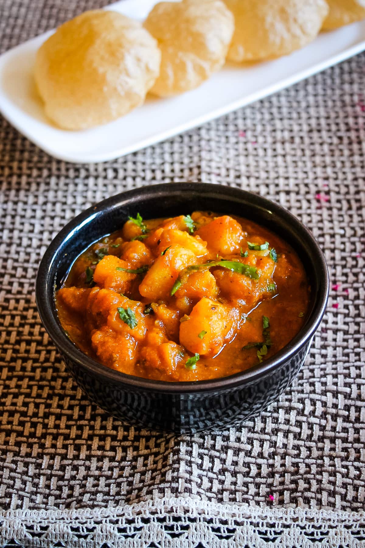 Potato gravy of aloo puri served in a bowl with puri in the back.