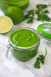 A glass jar of cilantro chutney with lime and cilantro in the back.