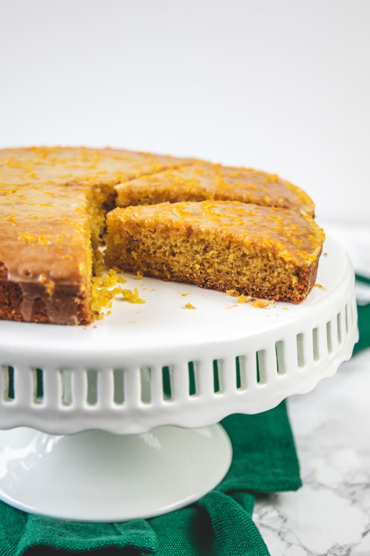 Orange cake on the cake stand with green napkin on side.