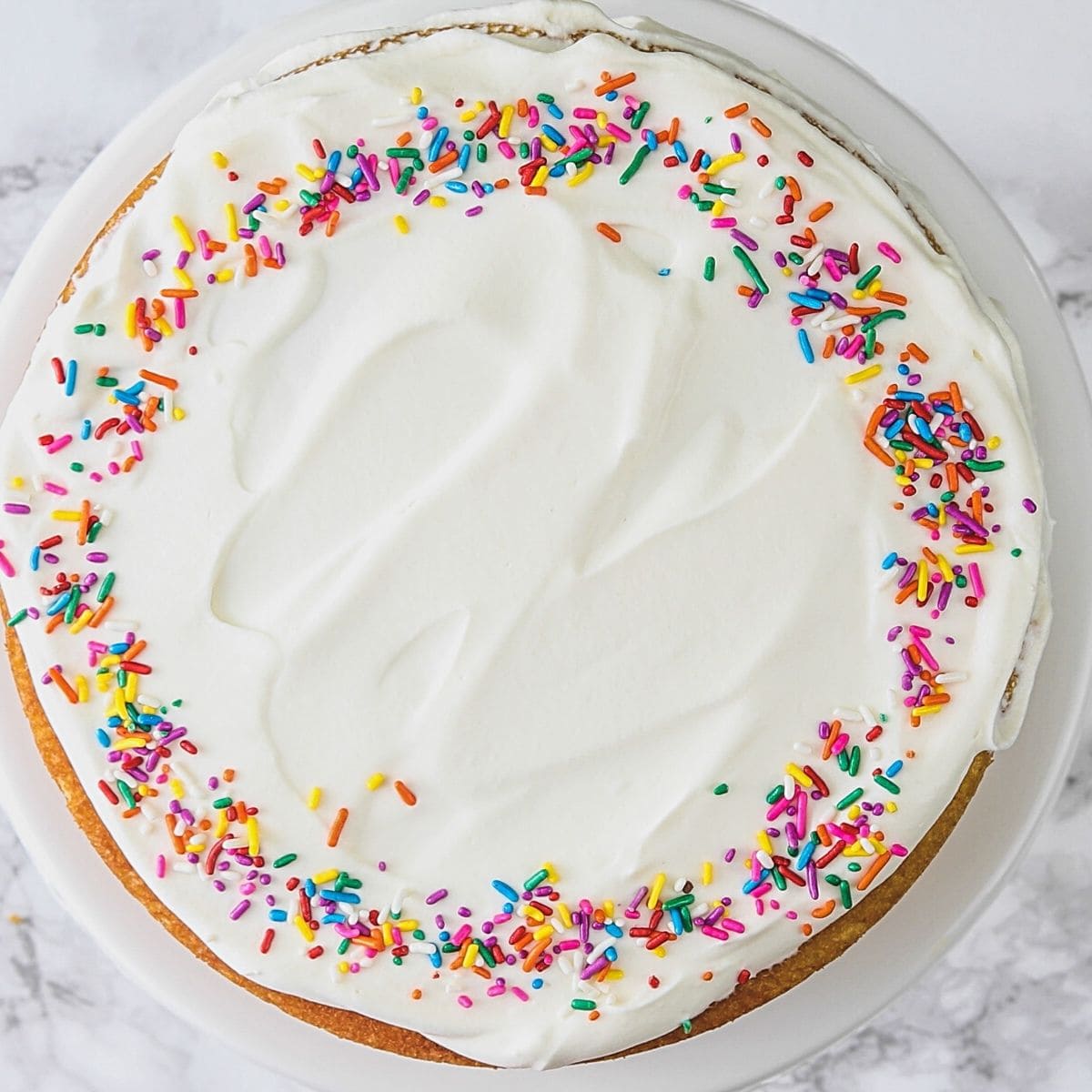 Top view of eggless vanilla cake frosted and decorated with sprinkles.