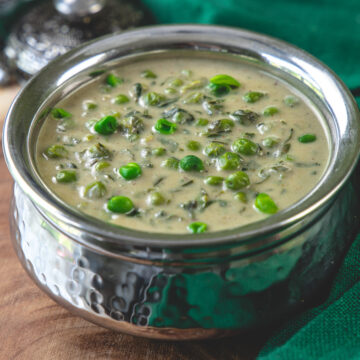 Methi matar malai in a steel serving bowl with green napkin on side.