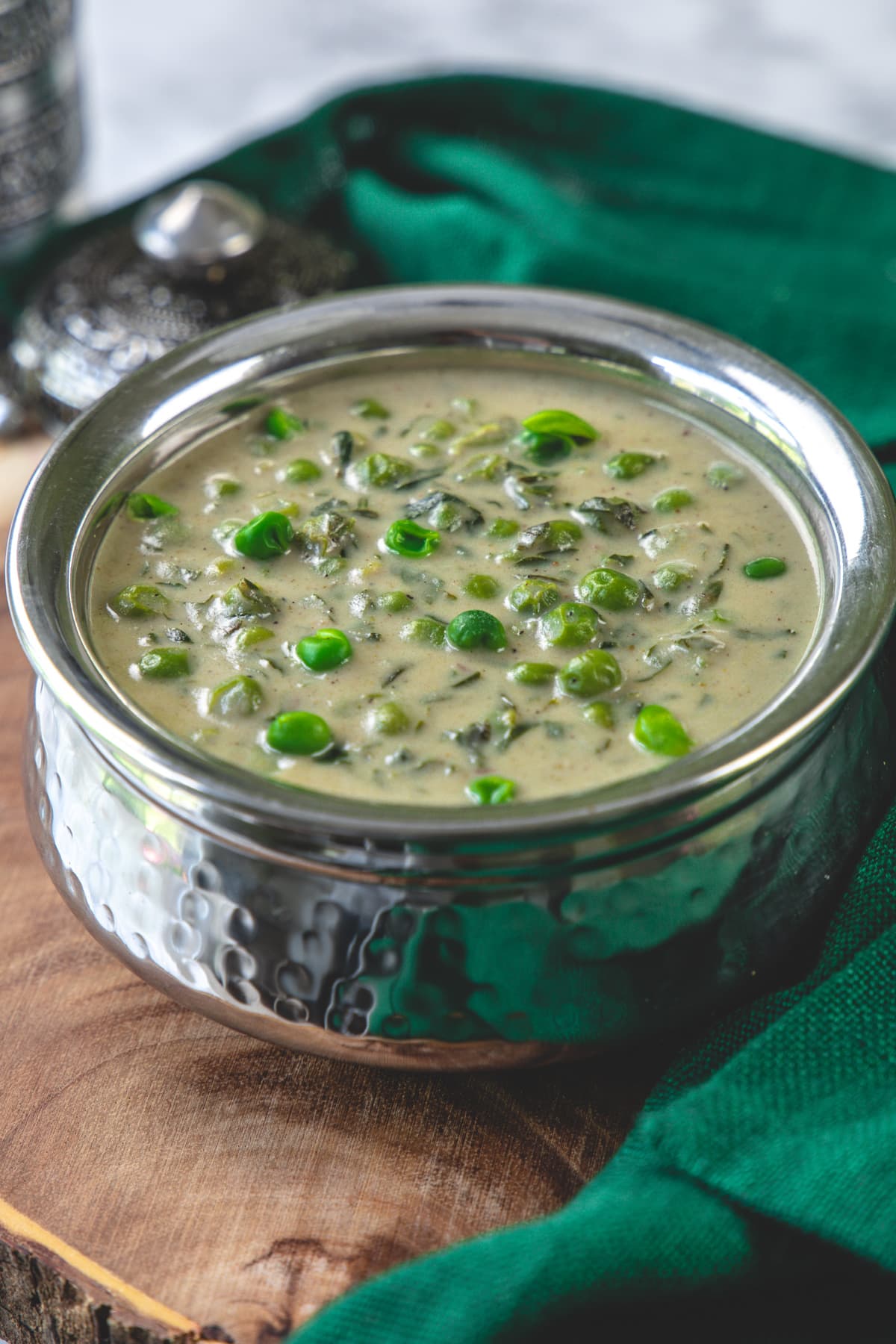 Methi matar malai in a steel serving bowl with green napkin on side.