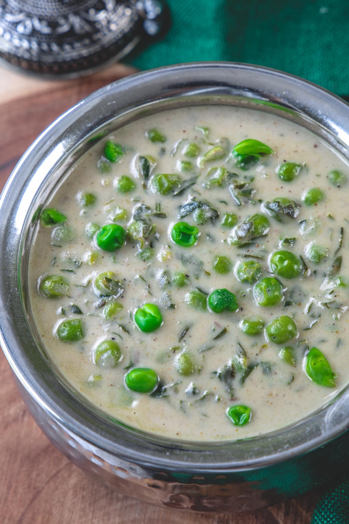 Close up pic of methi matar malai served in steel serving browl.