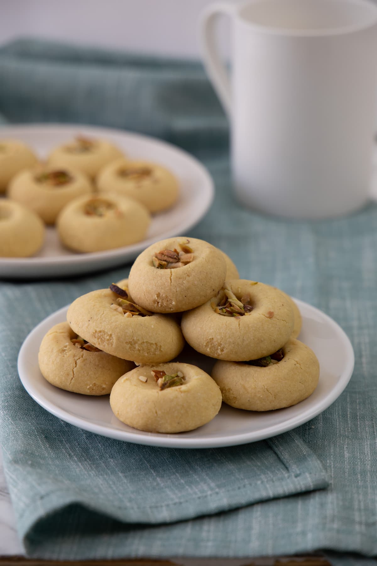 A stack of nankhatai cookies in a plate, few more in background with a cup of coffee.