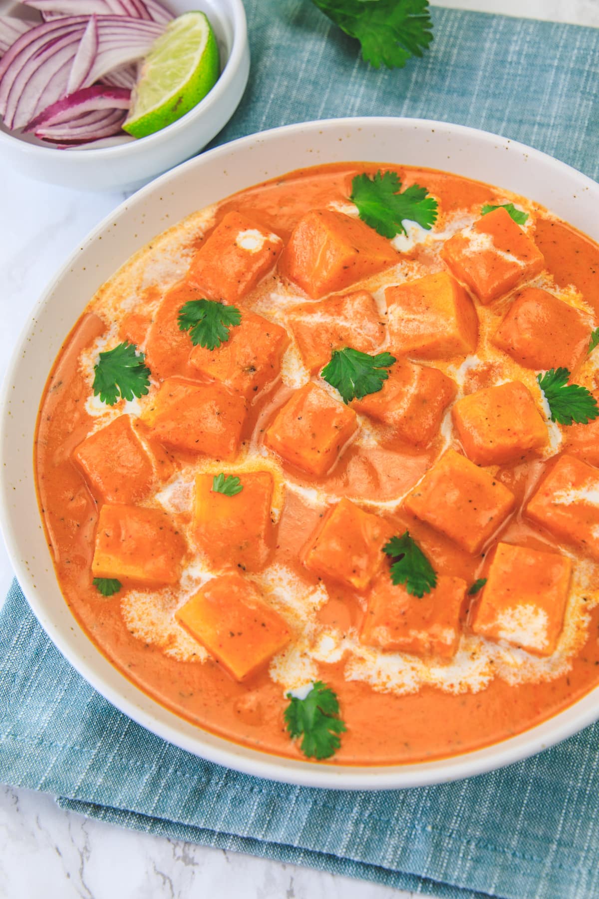 Close up of paneer makhani garnished with cilantro, napkin under the bowl.