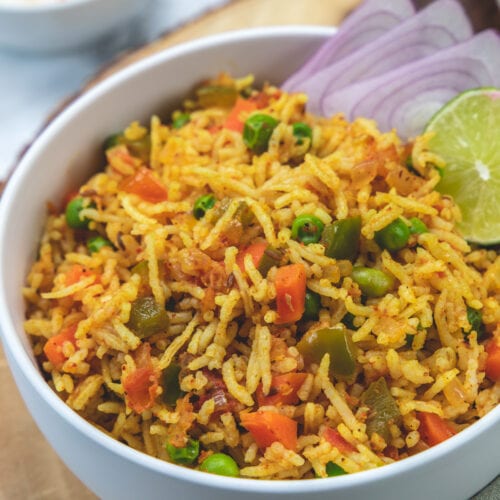 Tawa pulao in a bowl garnished with onion rings and lime wedge.