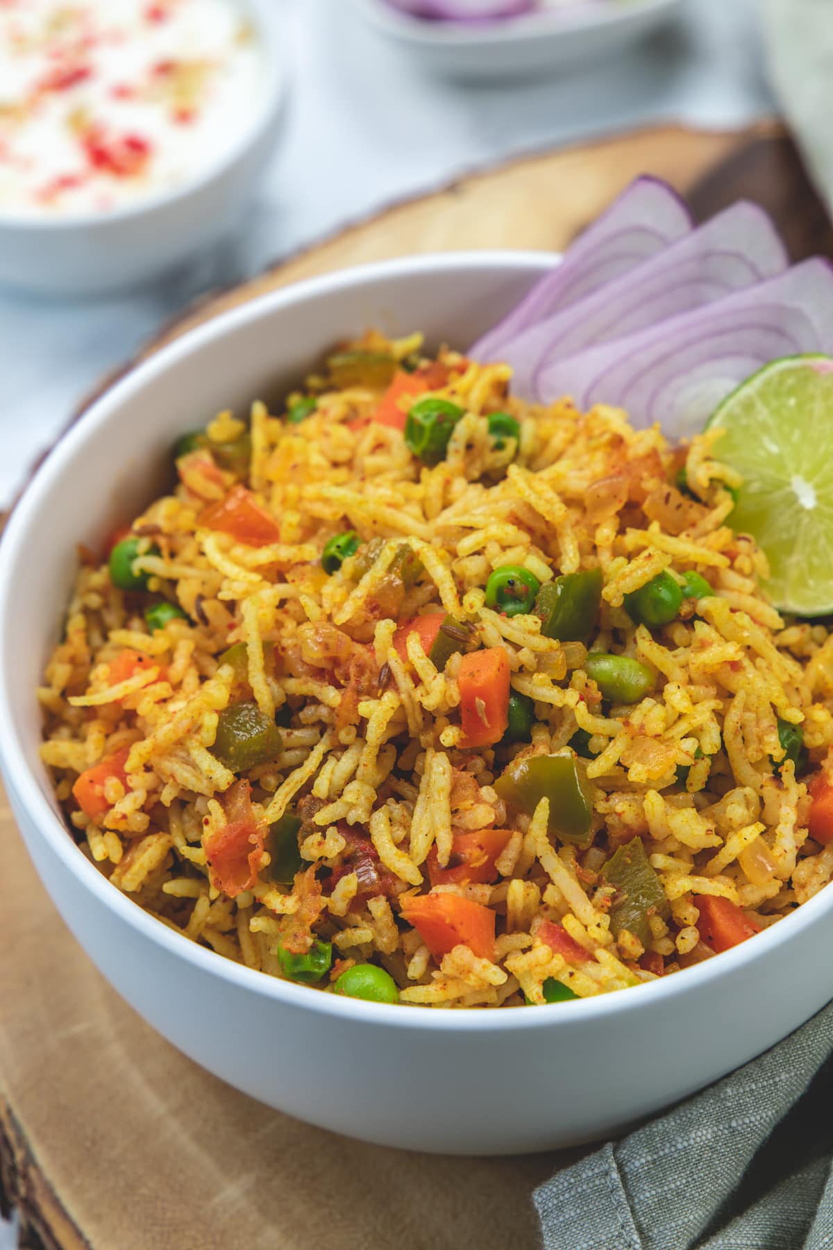 Tawa pulao in a bowl garnished with onion rings and lime wedge.