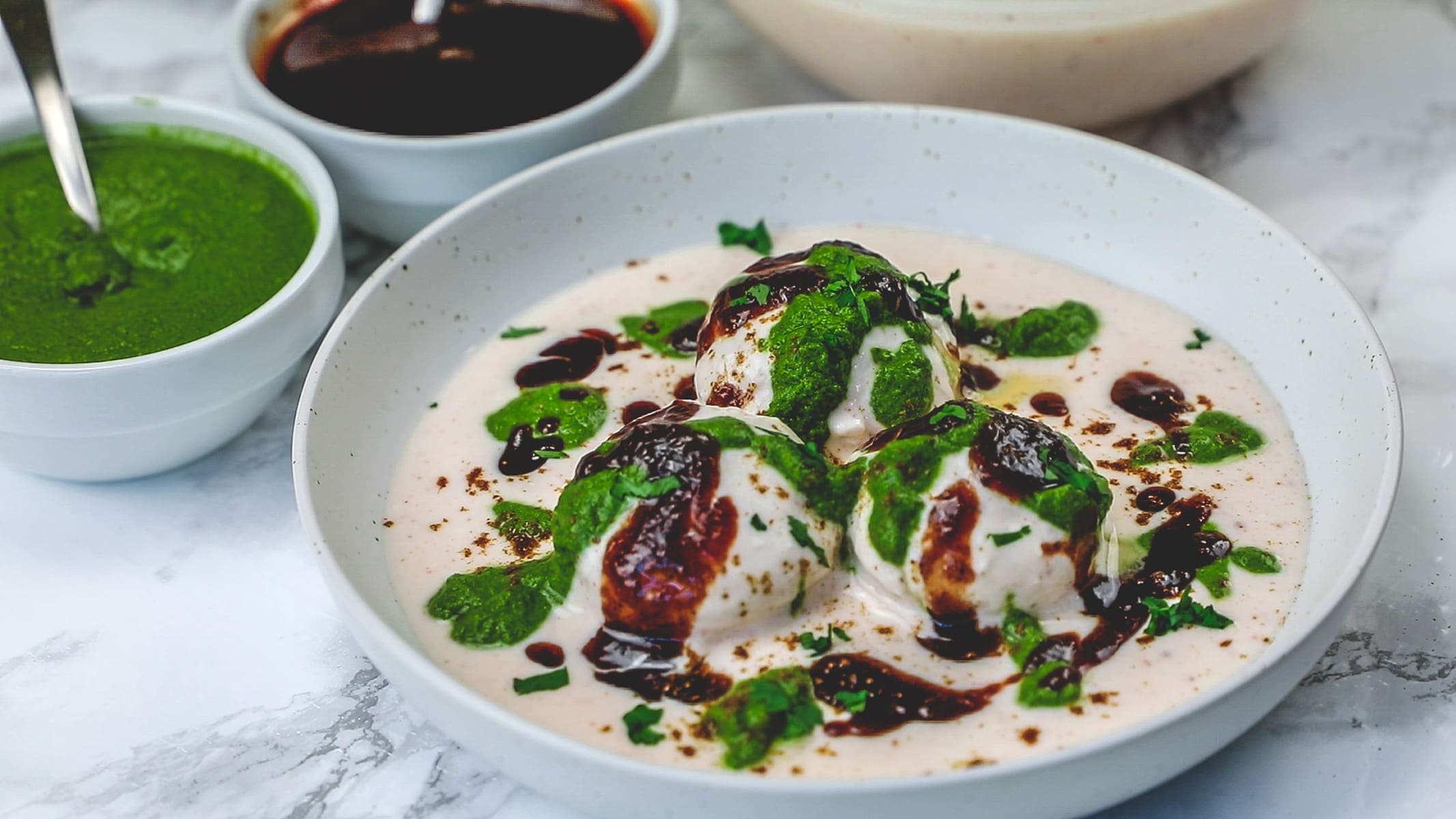 3 dahi vada in a plate drizzled with chutneys.