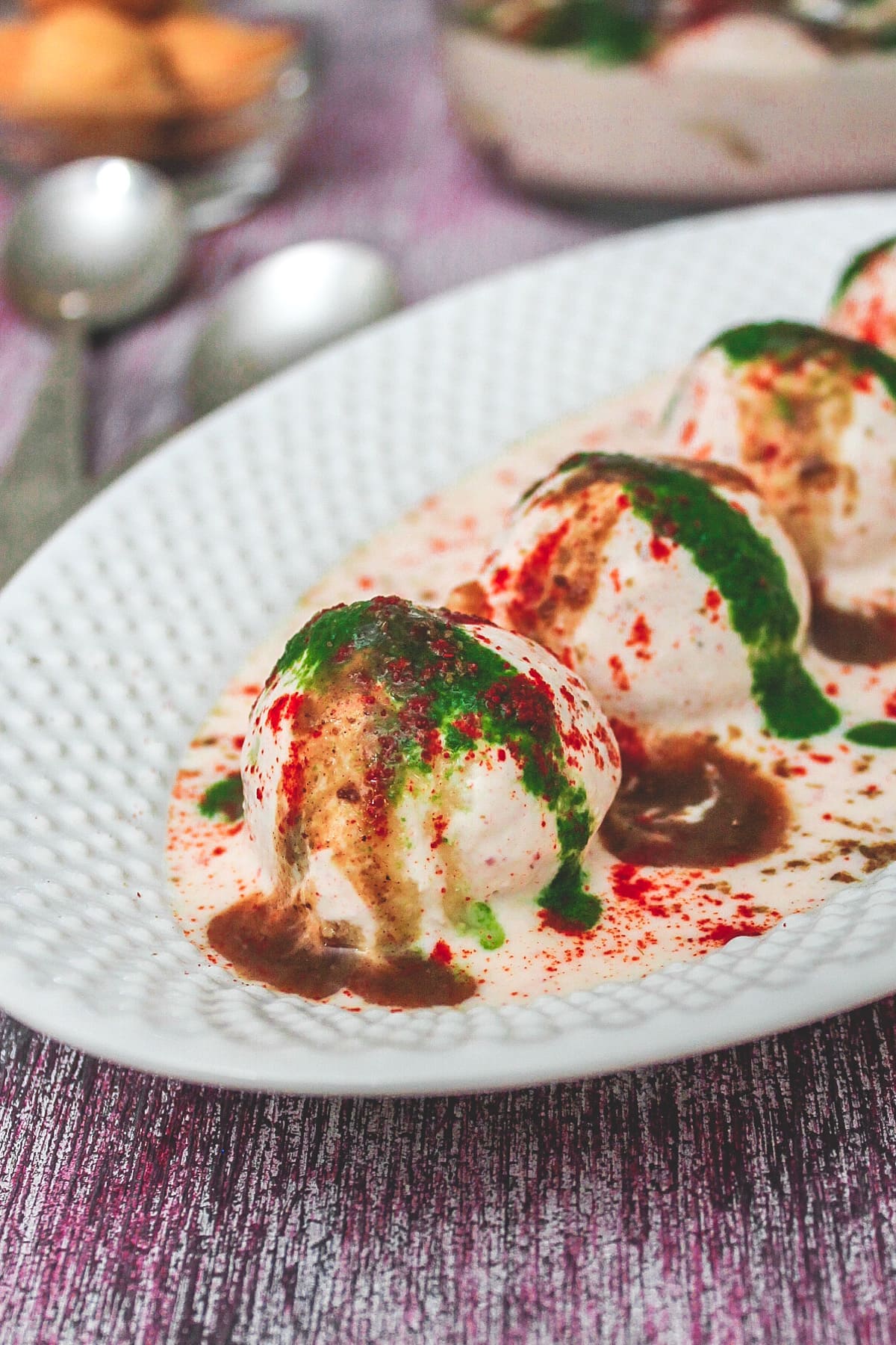 Close up of deep-fried dahi vada in an oval plate.