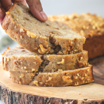 A stack of banana bread slices on a wooden board and taking away one slice.