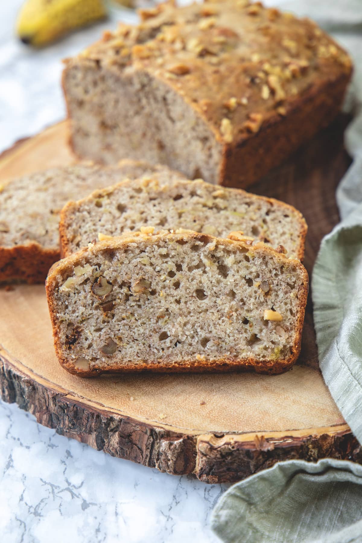 Slices on banana bread on wooden board with a napkin on side.