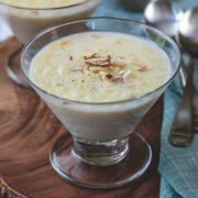 Two bowls of kheer garnished with nuts with napkin and spoons on the side.