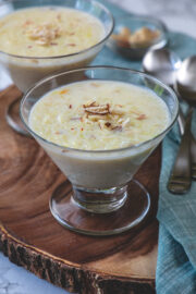 Two bowls of kheer garnished with nuts with napkin and spoons on the side.