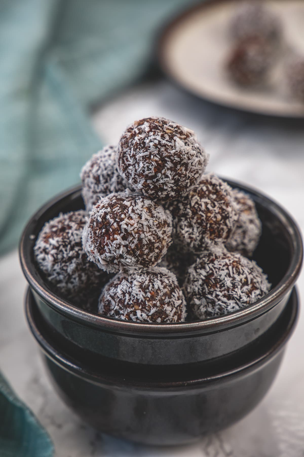 Stack of coconut date balls in a stack of 2 black bowls.