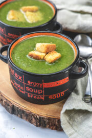 2 bowls of spinach soup topped with croutons with spoons and napkin on side.