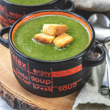 2 bowls of spinach soup topped with croutons with spoons and napkin on side.