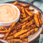 Air fryer sweet potato fries in a plate with a fry sauce in a bowl and napkin on the side.