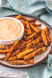 Air fryer sweet potato fries in a plate with a fry sauce in a bowl and napkin on the side.