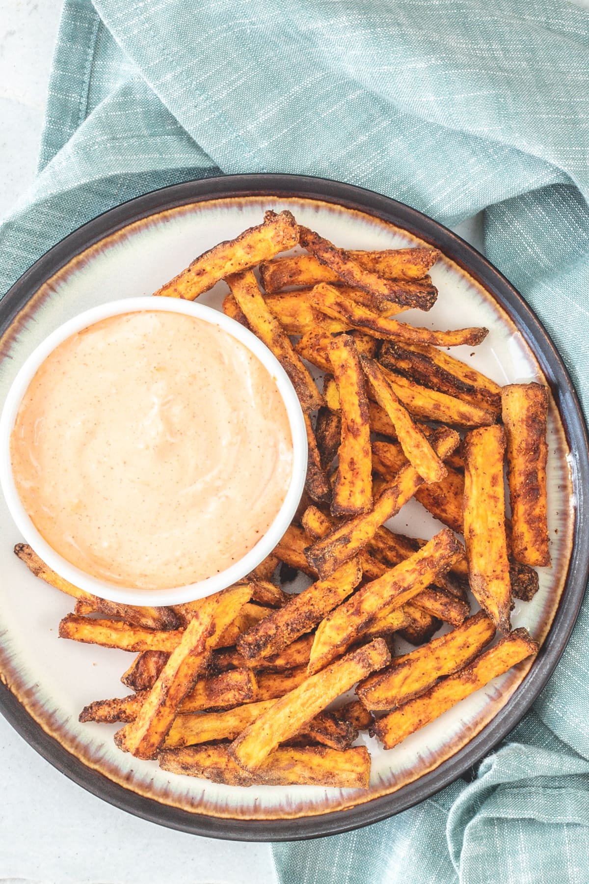 Top view of sweet potato fries in a plate with a fry sauce in a bowl.