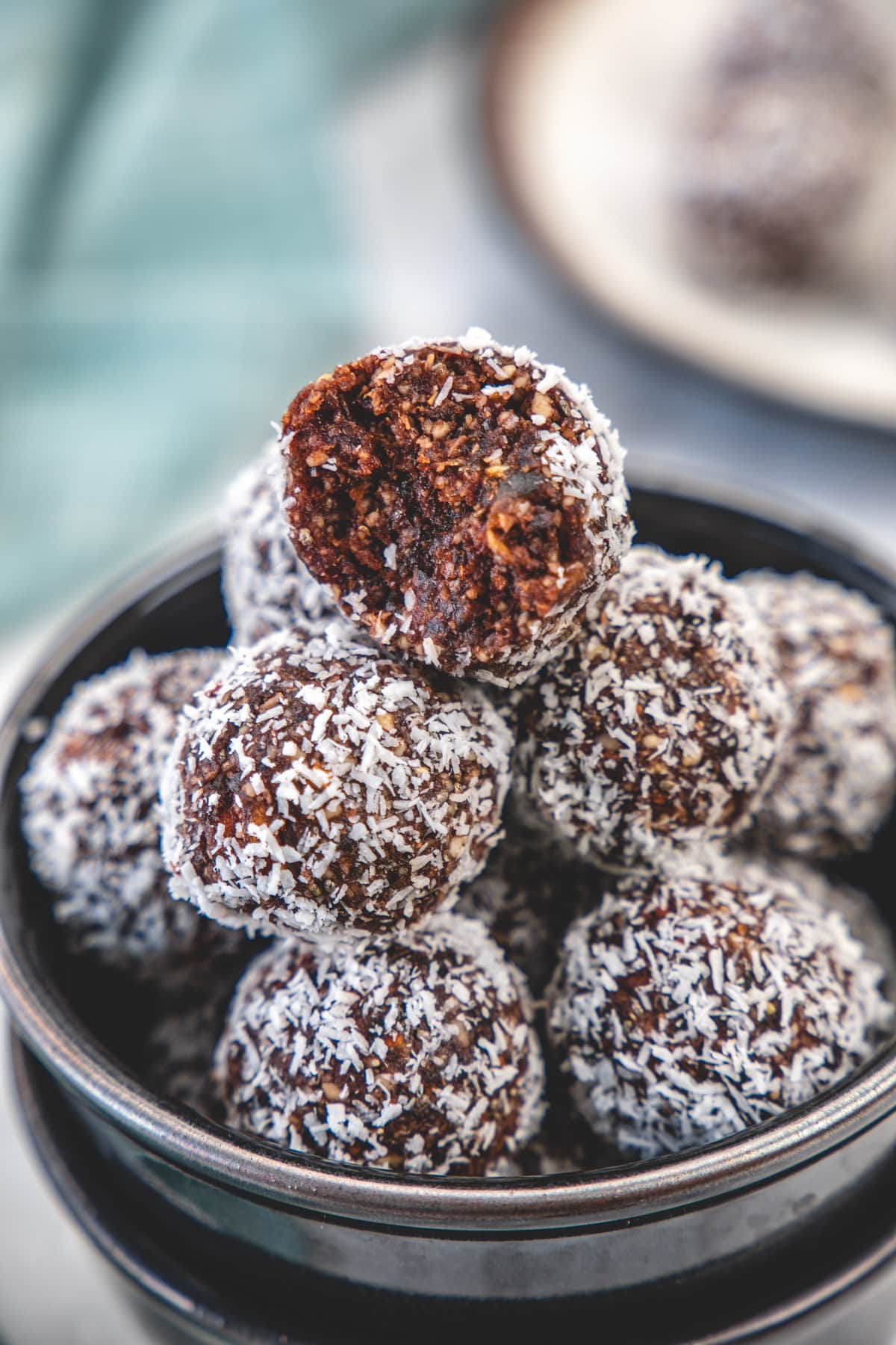 A bite is taken from a stack of date energy balls to show the inside texture.