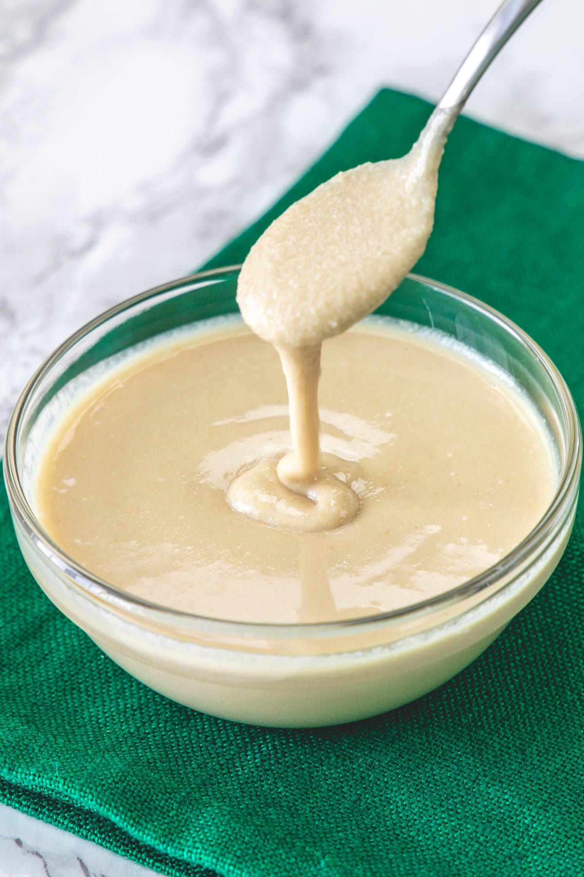 Drizzling tahini with a spoon back into the bowl to show texture.