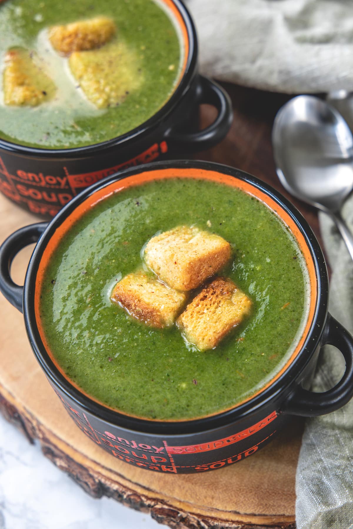 Close up of spinach soup in a bowl with croutons and another bowl in the back.