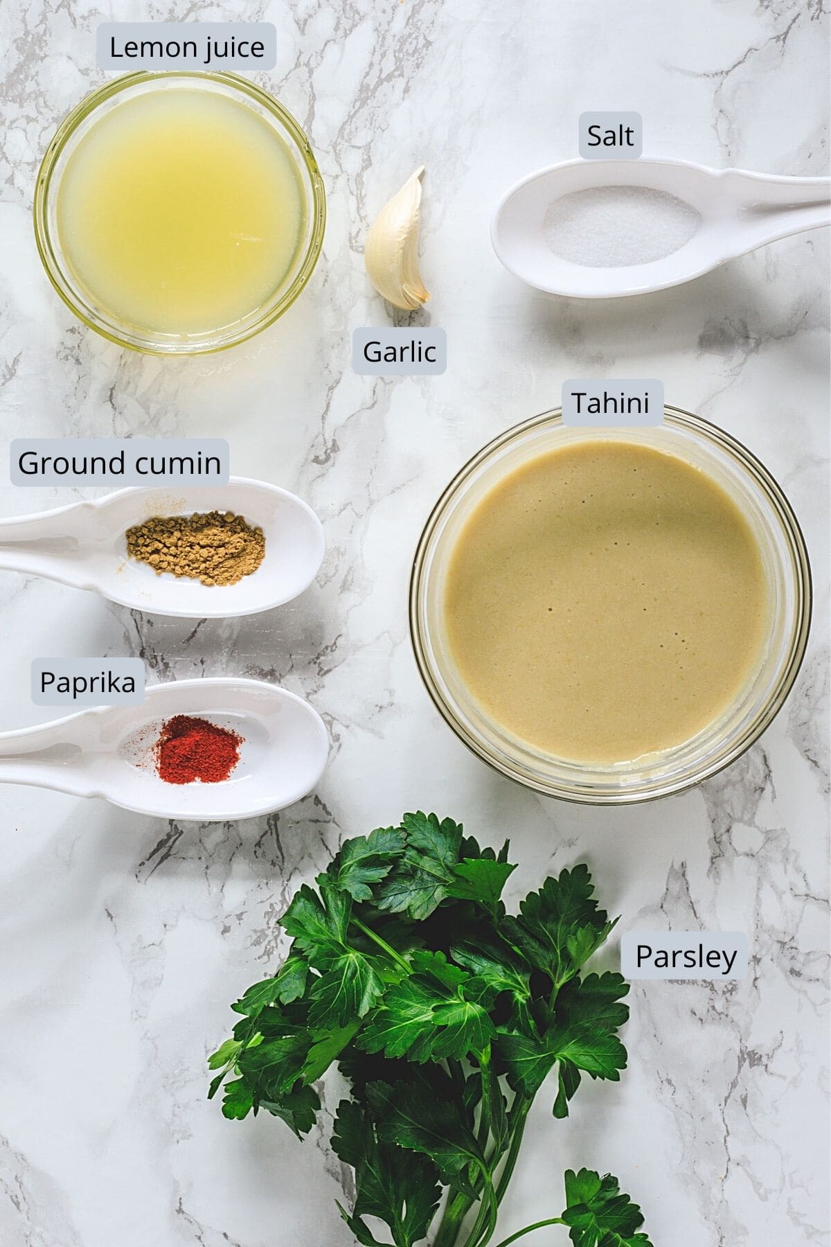 Ingredients used in tahini sauce in individual bowls and spoons.