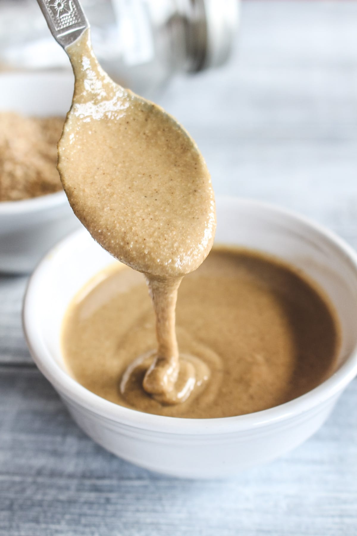 Drizziling tahini with a spoon back into a white bow.