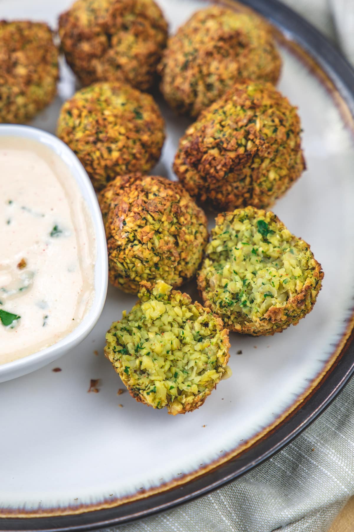 air fryer falafel cut into half to shown inside texture served with tahini sauce.