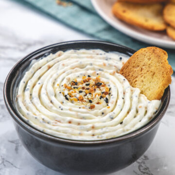 Everything bagel dip served in a black bowl with a crostini toast.