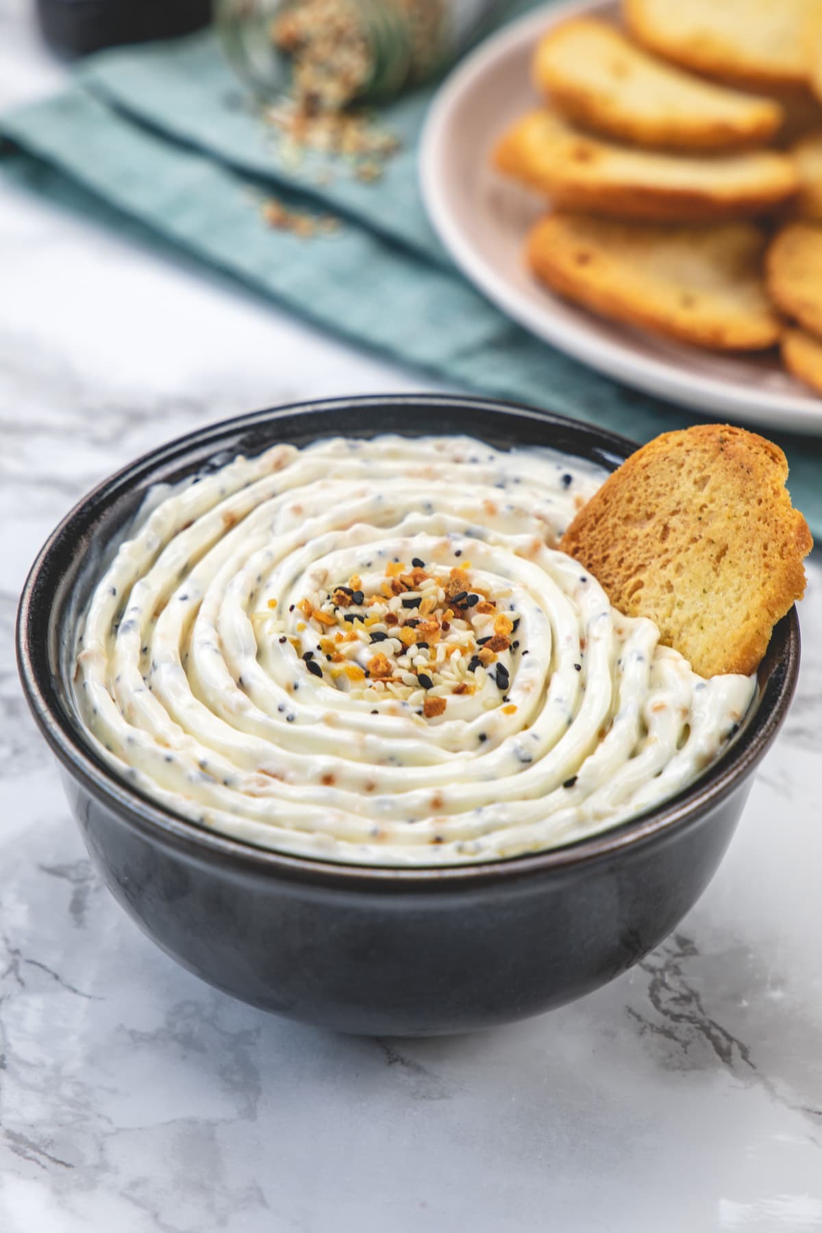 Everything bagel dip served in a black bowl with a crostini toast.