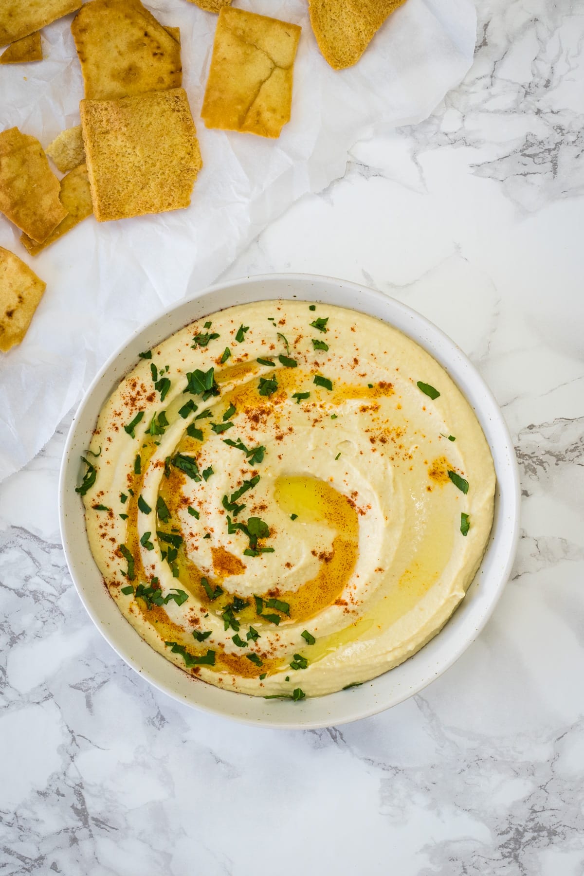 Top view of hummus served in a plate with drizzle of olive oil and paprika, served with chips.