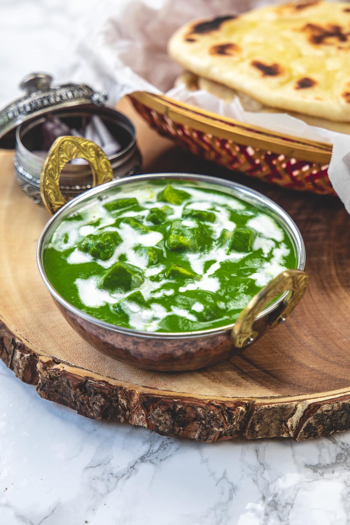 Palak paneer served in kadai with a garnish of cream and side of naan, onions.